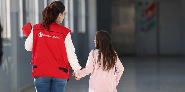 Lebanon, a Save the Children staff member in a red vest holds the hand of a child in a pink shirt. ch1959834-rec Lebanon, a Save the Children staff member in a red vest holds the hand of a child in a pink shirt. ch1959834-rec