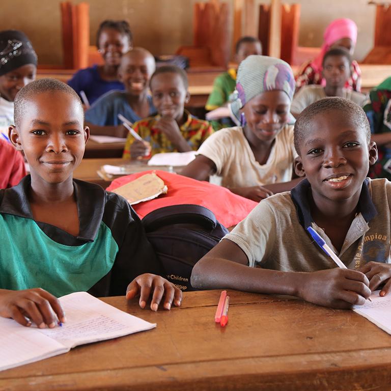 Children sitting at desks in a classroom in Mali, smiling at the camera while participating in Save the Children's education program. Children sitting at desks in a classroom in Mali, smiling at the camera while participating in Save the Children's education program.