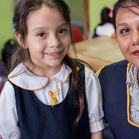 Marina and her teacher stand next to each other wearing school uniforms and smile. Marina and her teacher stand next to each other wearing school uniforms and smile.