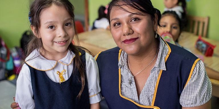 Marina and her teacher stand next to each other wearing school uniforms and smile. Marina and her teacher stand next to each other wearing school uniforms and smile.