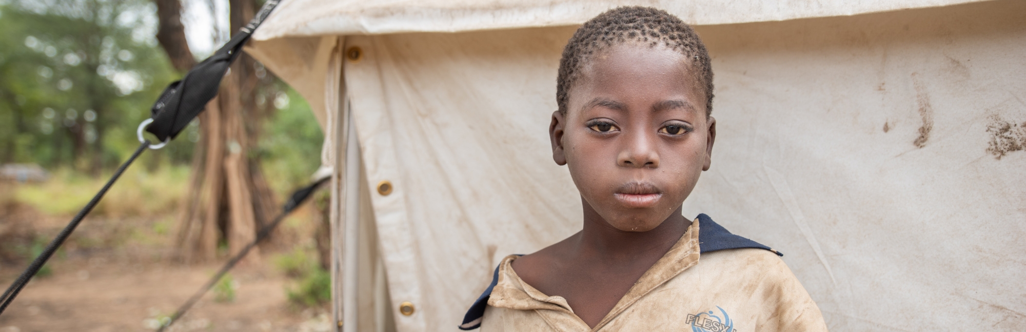 A ten-year old African child who lost his home when Cyclone Idai hit stands near a tent in Mozambique.