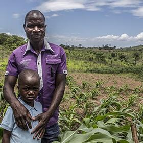 A father stands with his son in a field in Mozambique where he works to support his family A father stands with his son in a field in Mozambique where he works to support his family