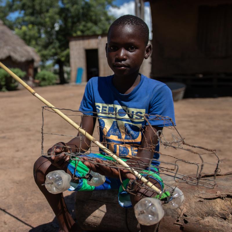 Eleven-year-old boy with the toy car he made from wire and bottle tops.