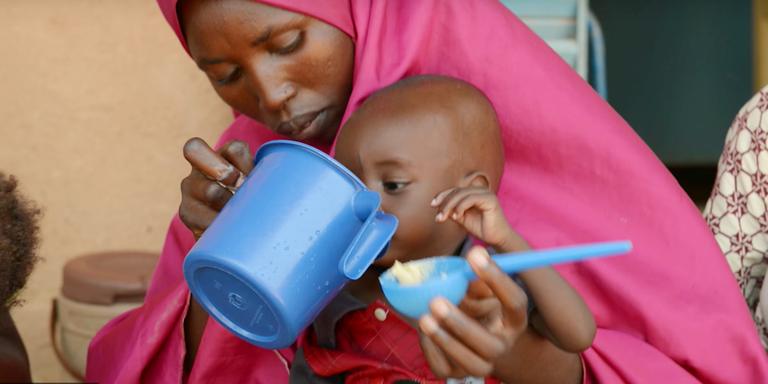 A woman feeds her child from a blue cup. A woman feeds her child from a blue cup.