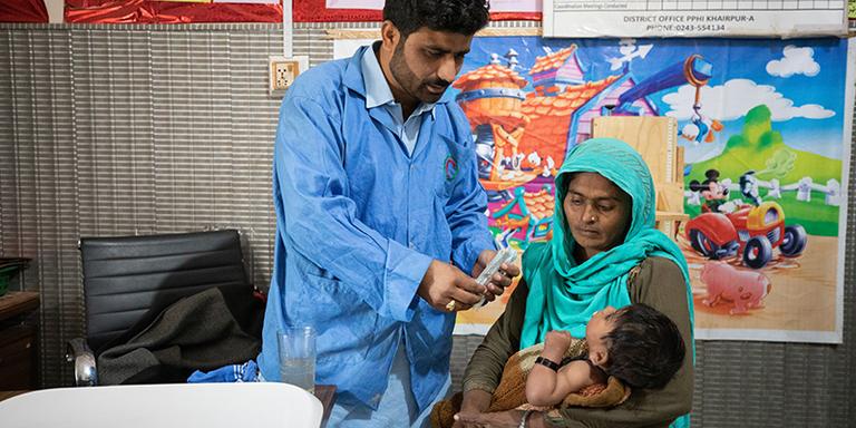 Pakistan, a mother holds her baby while a nutritional assistant helps feed her. ch1778084-rec Pakistan, a mother holds her baby while a nutritional assistant helps feed her. ch1778084-rec
