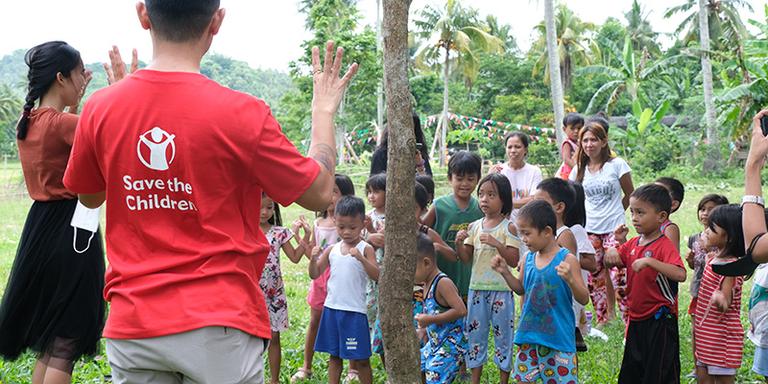 A group of young children in the Philippines watch Save the Children staff explaining a game A group of young children in the Philippines watch Save the Children staff explaining a game