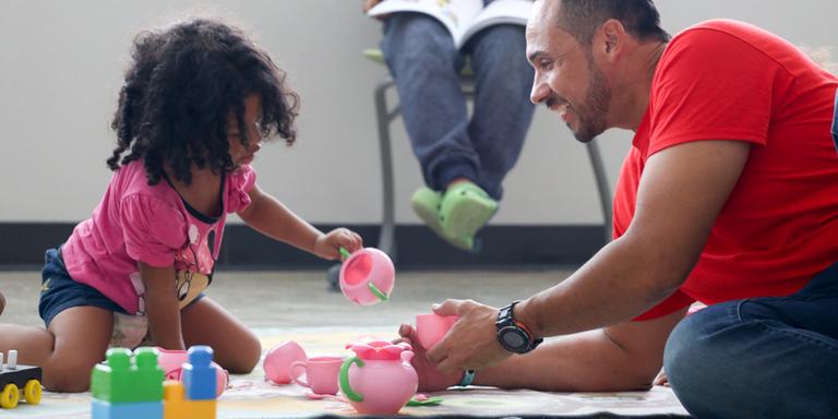 A Save the Children staff member plays with a young child in a child friendly space. A Save the Children staff member plays with a young child in a child friendly space.