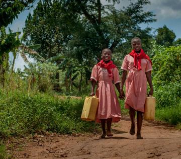 A girl and her friend holding water containers in Uganda. A girl and her friend holding water containers in Uganda.