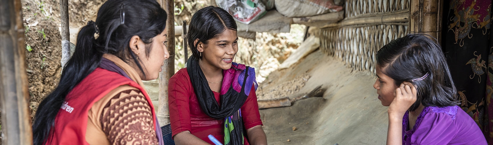 A Save the Children staff member sits with two adolescent girls.