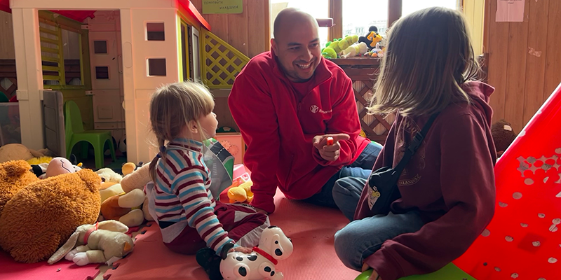 A Save the Children staffer sits with two little girls in a child friendly space in Bucharest, Romania