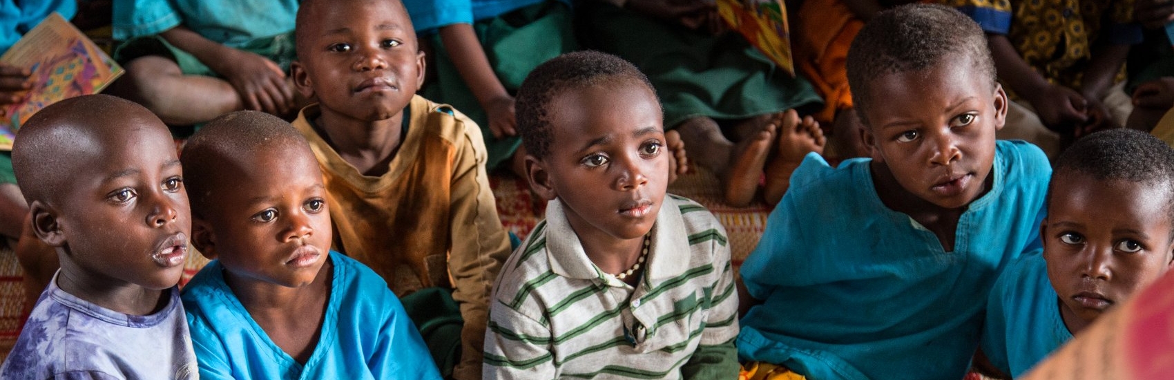 Children at the Kiboga Early Childhood Care and Development (ECCD) center in Burera, Rwanda listen as a caregiver reads aloud to them from a book that was provided through Save the Children's support. These structured sessions are part of early literacy activities featured in Save the Children's Signature Education Program, which combines teacher training, assessments, community action, innovating classroom designs, and support for the publishing of children's books in order to increase literacy in Rwanda. 