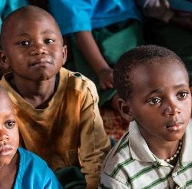 Children at the Kiboga Early Childhood Care and Development (ECCD) center in Burera, Rwanda listen as a caregiver reads aloud to them from a book that was provided through Save the Children's support. These structured sessions are part of early literacy activities featured in Save the Children's Signature Education Program, which combines teacher training, assessments, community action, innovating classroom designs, and support for the publishing of children's books in order to increase literacy in Rwanda. Children at the Kiboga Early Childhood Care and Development (ECCD) center in Burera, Rwanda listen as a caregiver reads aloud to them from a book that was provided through Save the Children's support. These structured sessions are part of early literacy activities featured in Save the Children's Signature Education Program, which combines teacher training, assessments, community action, innovating classroom designs, and support for the publishing of children's books in order to increase literacy in Rwanda.
