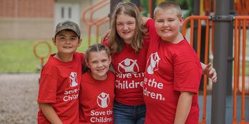 In West Virginia, a group of four school-age children stand together on a sunny summer day, in front of a playground. In West Virginia, a group of four school-age children stand together on a sunny summer day, in front of a playground.