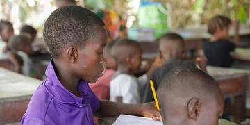 A boy sits at a desk in a classroom solving a math problem in Sierra Leone. A boy sits at a desk in a classroom solving a math problem in Sierra Leone.