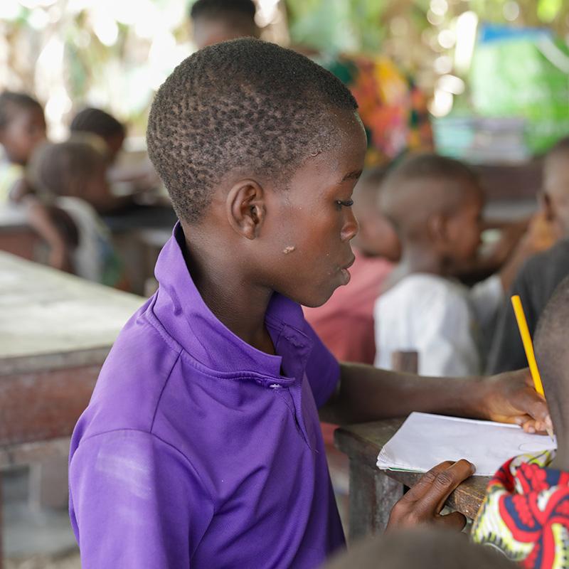 A boy sits at a desk in a classroom solving a math problem in Sierra Leone.