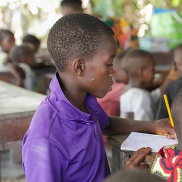 A boy sits at a desk in a classroom solving a math problem in Sierra Leone. A boy sits at a desk in a classroom solving a math problem in Sierra Leone.