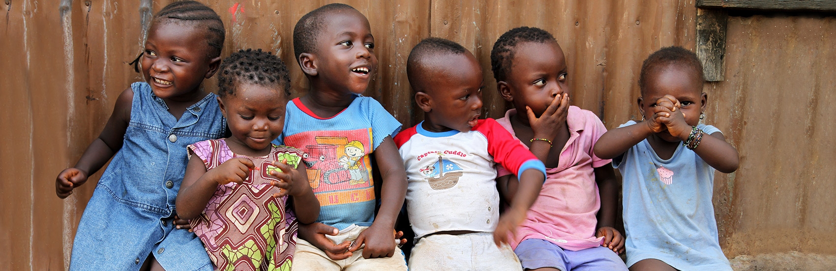 Six young girls and boys smile and giggle as they sit closely together at The Children’s Club in Kroo Bay, Sierra Leone. The Children’s Club was formed by Save the Children in 2007 as a means of protecting children and teaching them, and their communities, about children’s rights. The Clubs give children confidence and knowledge of their rights, and empower children to become role models for their own generation and those to come. The Clubs are open to every child. Photo credit: Anne-Sofie Helms/Save the Ch
