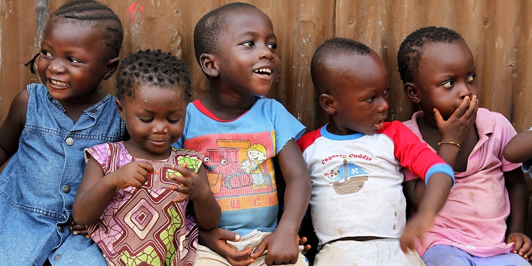 Six young girls and boys smile and giggle as they sit closely together at The Children’s Club in Kroo Bay, Sierra Leone. The Children’s Club was formed by Save the Children in 2007 as a means of protecting children and teaching them, and their communities, about children’s rights. The Clubs give children confidence and knowledge of their rights, and empower children to become role models for their own generation and those to come. The Clubs are open to every child. Photo credit: Anne-Sofie Helms/Save the Ch