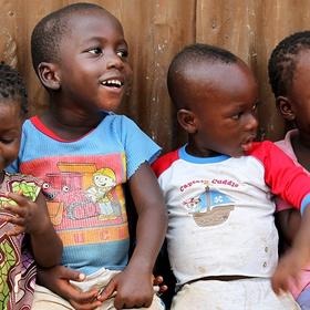 Six young girls and boys smile and giggle as they sit closely together at The Children’s Club in Kroo Bay, Sierra Leone. The Children’s Club was formed by Save the Children in 2007 as a means of protecting children and teaching them, and their communities, about children’s rights. The Clubs give children confidence and knowledge of their rights, and empower children to become role models for their own generation and those to come. The Clubs are open to every child. Photo credit: Anne-Sofie Helms/Save the Ch Six young girls and boys smile and giggle as they sit closely together at The Children’s Club in Kroo Bay, Sierra Leone. The Children’s Club was formed by Save the Children in 2007 as a means of protecting children and teaching them, and their communities, about children’s rights. The Clubs give children confidence and knowledge of their rights, and empower children to become role models for their own generation and those to come. The Clubs are open to every child. Photo credit: Anne-Sofie Helms/Save the Ch