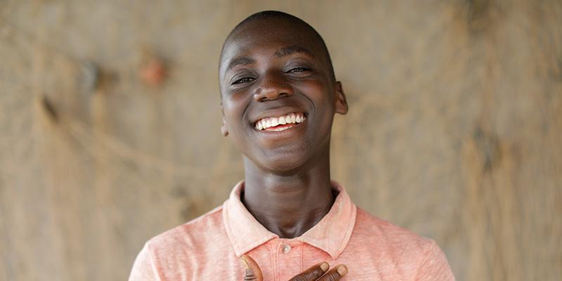 A boy stands smiling at the camera wearing an orange shirt