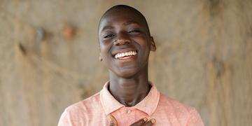 A boy stands smiling at the camera wearing an orange shirt A boy stands smiling at the camera wearing an orange shirt