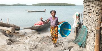 A girl stands by the ocean outside her house holding a wash basin in Sierra Leone. A girl stands by the ocean outside her house holding a wash basin in Sierra Leone.