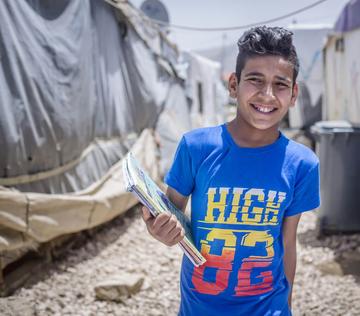 A 13-year old boy stands with his school books outdoors in an informal tented settlement in Lebanon. A 13-year old boy stands with his school books outdoors in an informal tented settlement in Lebanon.