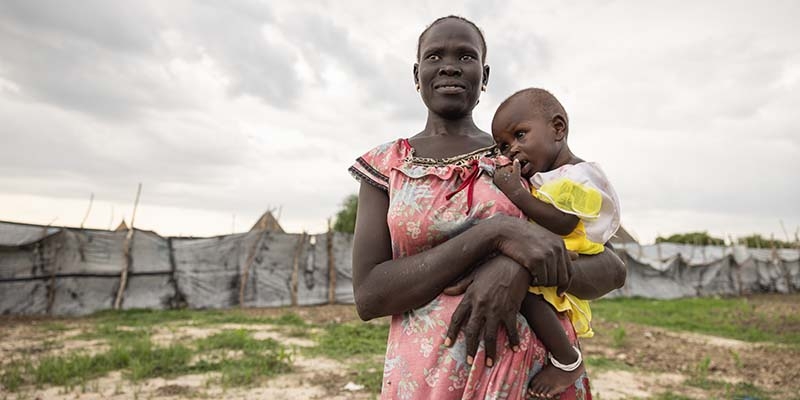 In South Sudan, a woman stands outside and looks into the distance while holding her child in her arms. In South Sudan, a woman stands outside and looks into the distance while holding her child in her arms.