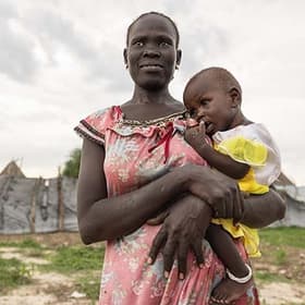 In South Sudan, a woman stands outside and looks into the distance while holding her child in her arms. In South Sudan, a woman stands outside and looks into the distance while holding her child in her arms.