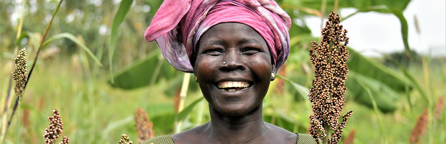 A South Sudanese farmer smiles standing among her crops