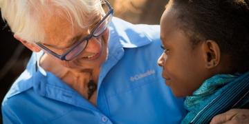 A woman in a blue shirt and glasses smiles at a young girl A woman in a blue shirt and glasses smiles at a young girl