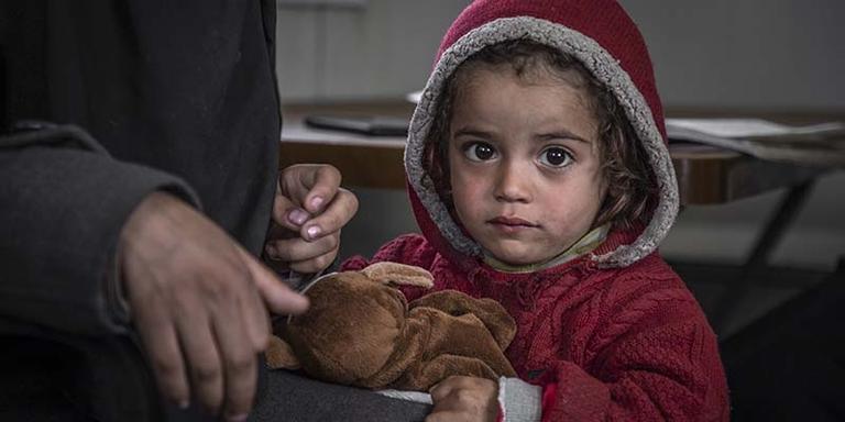 In Syria, a child caught in the crossfire of conflict stands against a stark background. In Syria, a child caught in the crossfire of conflict stands against a stark background.