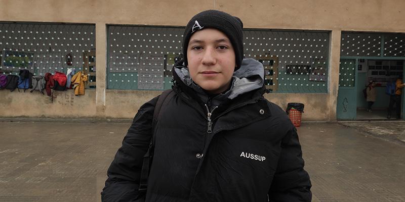A boy wears a black ski cap and a black winter jacket