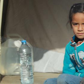 Syria, a young girl in a teal sweater sits in the entrance of her family's tent. Syria, a young girl in a teal sweater sits in the entrance of her family's tent.