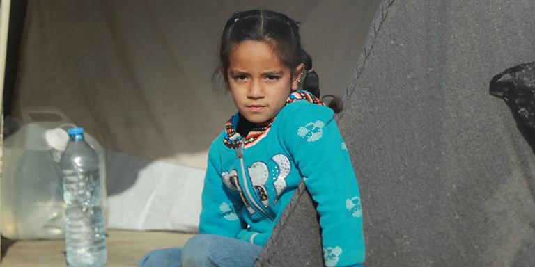 Syria, a young girl in a teal sweater sits in the entrance of her family's tent. Syria, a young girl in a teal sweater sits in the entrance of her family's tent.