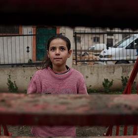 In Syria, a girl stands in front of a building that has been destroyed. In Syria, a girl stands in front of a building that has been destroyed.