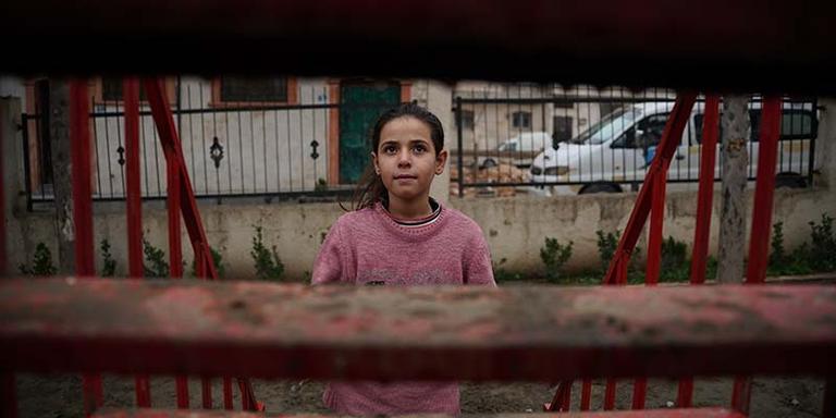 In Syria, a girl stands in front of a building that has been destroyed. In Syria, a girl stands in front of a building that has been destroyed.