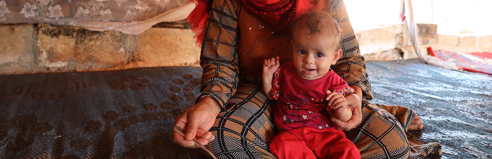 Rafqa*, 40, prepares to feed her 10 month old daughter Hana* in their tent in Syria Rafqa*, 40, prepares to feed her 10 month old daughter Hana* in their tent in Syria