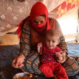 Rafqa*, 40, prepares to feed her 10 month old daughter Hana* in their tent in Syria Rafqa*, 40, prepares to feed her 10 month old daughter Hana* in their tent in Syria