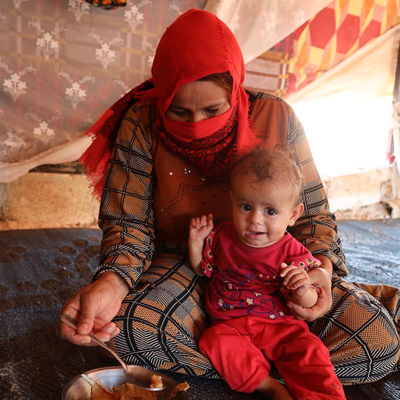 Rafqa*, 40, prepares to feed her 10 month old daughter Hana* in their tent in Syria Rafqa*, 40, prepares to feed her 10 month old daughter Hana* in their tent in Syria