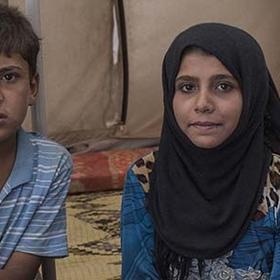 Two young siblings sit together in a tent in a refugee camp in Syria. Two young siblings sit together in a tent in a refugee camp in Syria.