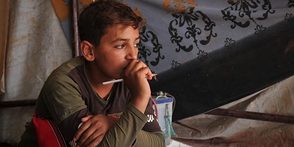 Syria, a boy in a striped shirt holds a pen looking away from the camera. Syria, a boy in a striped shirt holds a pen looking away from the camera.