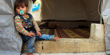 A two-year-old girl sits on the floor of her family’s tent in a camp for displaced people on the northern Syrian border. Photo credit: Ahmad Baroudi/Save the Children, May 2015. A two-year-old girl sits on the floor of her family’s tent in a camp for displaced people on the northern Syrian border. Photo credit: Ahmad Baroudi/Save the Children, May 2015.