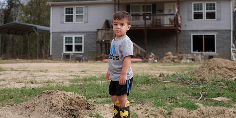 A young boy stands in the backyard of a house A young boy stands in the backyard of a house