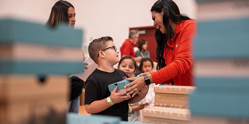 A boy holds a box of TOMS shoes handed to him by a Save the Children volunteer