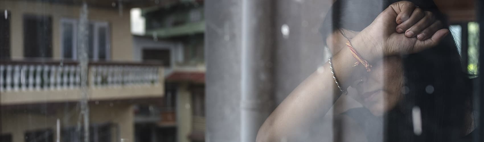 A girl who experienced child trafficking stands with her face covered in front of a window. 