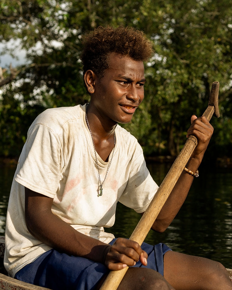 A teenage boy who lives in the Solomon Islands paddles a boat on the water. A teenage boy who lives in the Solomon Islands paddles a boat on the water.
