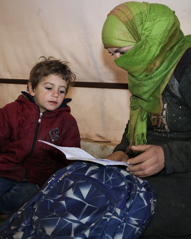 A young boy in Syria sits with his mother looking at schoolwork A young boy in Syria sits with his mother looking at schoolwork