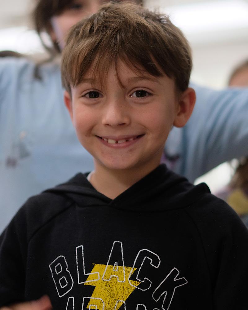 A boy smiles at the camera wearing a black sweatshirt