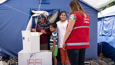 A family unpacks boxes in front of a tent with a Save the Children staffer in Turkey A family unpacks boxes in front of a tent with a Save the Children staffer in Turkey
